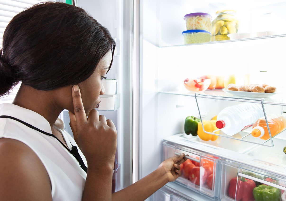 Mulher olhando para a geladeira aberta enquanto escolher o que vai comer