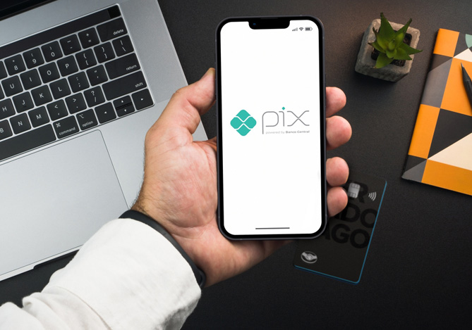 Mão de uma pessoa segurando um celular com símbolo do Pix com cartão de crédito, uma nova funcionalidade que você aproveita no Mercado Pago. 