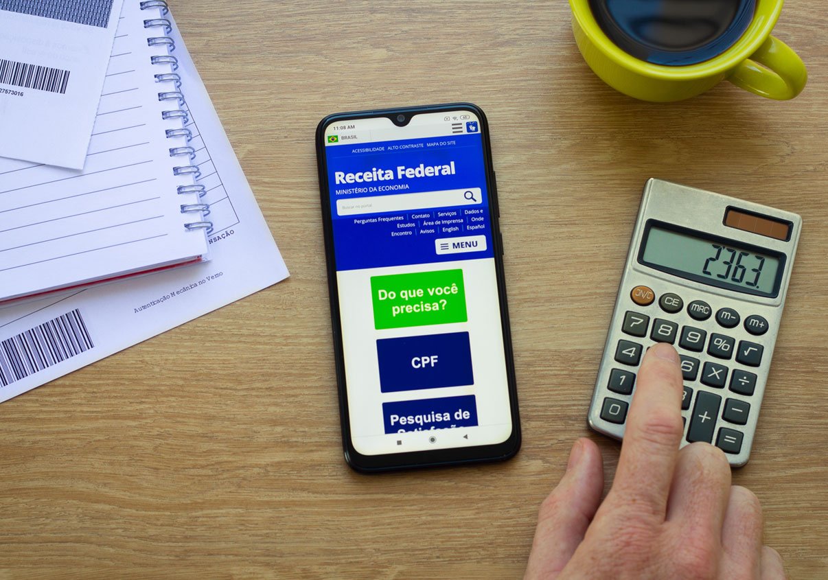 Pessoa usando a calculadora e o celular para fazer o cálculo da sua Restituição do Imposto de Renda