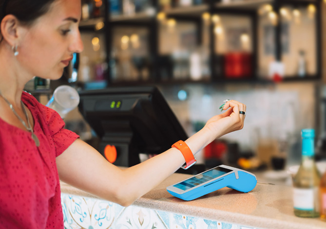Mulher fazendo pagamentos por aproximação com smartwatch na maquininha de cartão Point do Mercado Pago