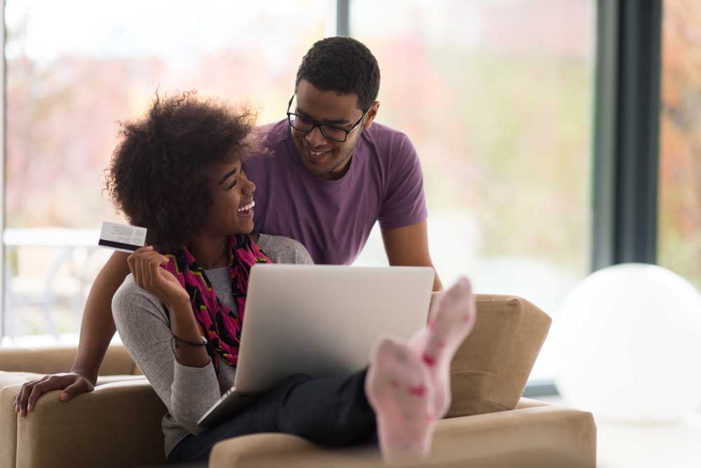 Um casal de compradores com o notebook aberto analisando o que irão comprar na internet