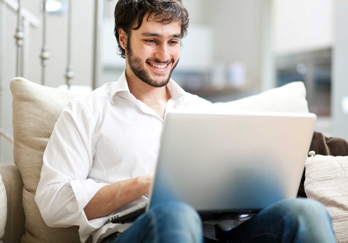 Homem sorrindo sentado no sofá e com um laptop no colo